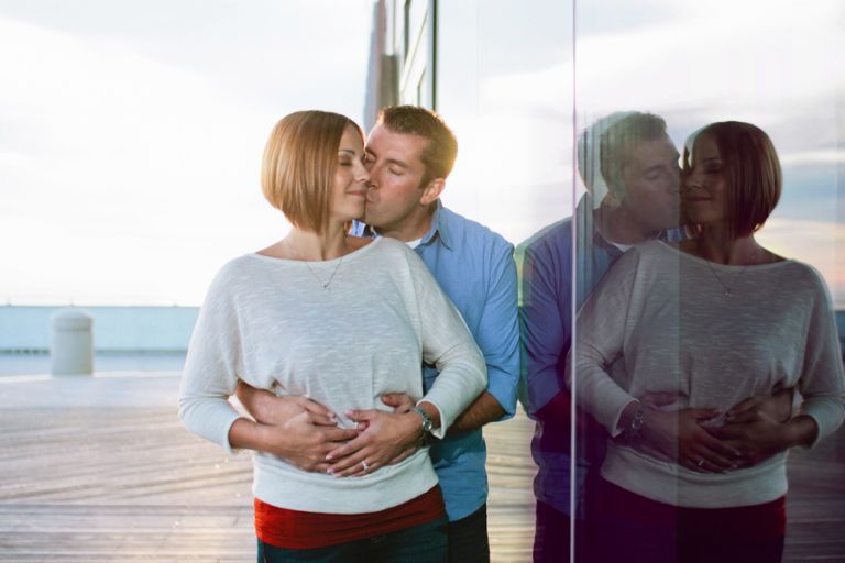 couple embraces on Atlantic City Pier next to their reflection in glass during their engagement photo session with their wedding photographers